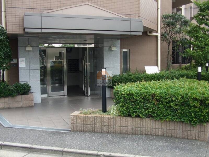 藤和シティホームズ西日暮里 (2)｜エントランス正面は、ガラス扉と石調タイルの壁面で構成され、清潔感と堅牢性を兼備。周囲の植栽が四季を彩り、住まいとしての品格を高めている。